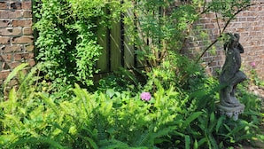 Ein Garten mit Backsteinmauer, Holzpflanzzaun und einer Statue.