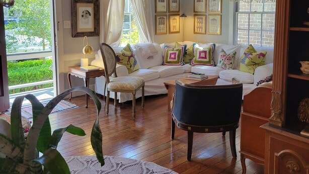 Ein gemütliches Wohnzimmer mit einer Holztreppe, einem weißen Sofa mit bunten Kissen, einem Esstisch mit weißen Tischdecken und einer Kristallleuchter.