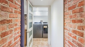 Un pasillo estrecho con paredes de ladrillo que conduce a un área de lavandería con electrodomésticos de acero inoxidable.