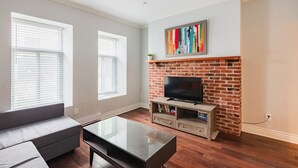 Una sala de estar con chimenea de ladrillo, un televisor de pantalla plana, un sofá gris y una mesa de centro de vidrio.