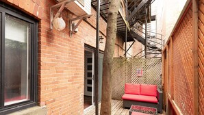 Un callejón estrecho con un muro de ladrillo, un árbol de madera, un banco rojo y una escalera.