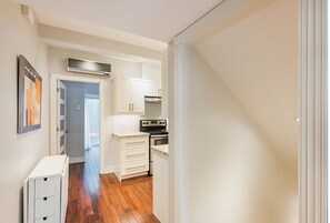 Un pasillo estrecho con una zona de cocina que cuenta con armarios blancos, una estufa y un horno.
