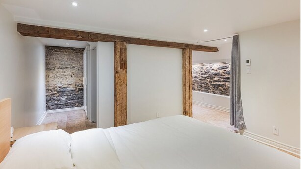Un dormitorio con una cama grande, vigas de madera, paredes de piedra y vistas del exterior de piedra.