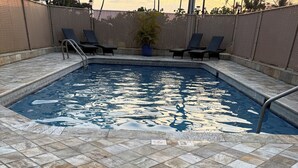 Une piscine avec une terrasse carrelée, des chaises longues et une clôture.