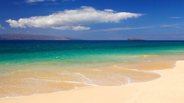 Une plage à l’eau turquoise et limpide, bordée d’un rivage sablonneux.