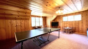 Una habitación con mesa de ping pong, televisor y comedor con sillas y una mesa.