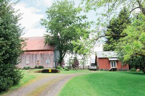 A rural barn with a gravel path leading to it, surrounded by lush greenery and trees.
