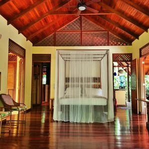 A room with a wooden ceiling, a bed with a canopy, a chair, and a view of the outdoors.