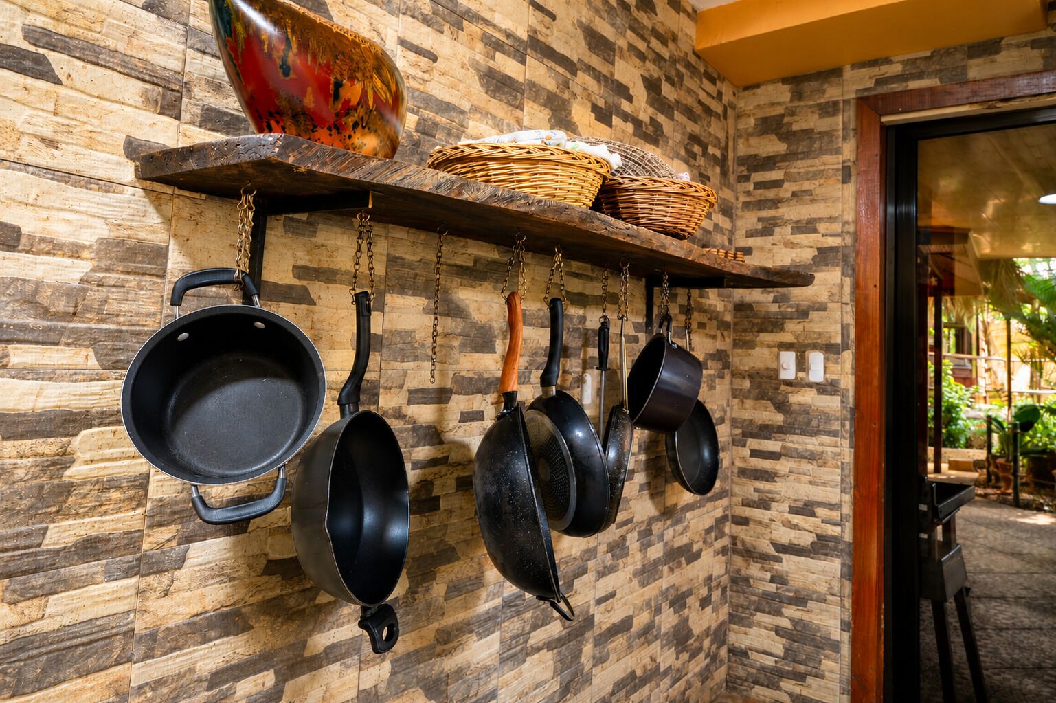 Een keuken met hangende pannen en potten, een houten plank met manden, en een muur met een stenen patroon.