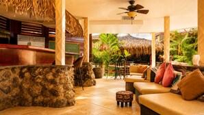A tropical lounge area with stone columns, a bar, and outdoor seating. - Casa Melosa Villa in Playa Potrero/Flamingo Costa Rica (Playa Potrero/Flamingo)