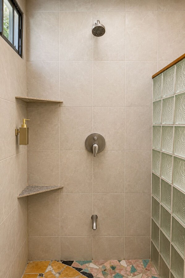 A shower with a handheld showerhead, a wall-mounted faucet, and a tiled floor with a geometric pattern.