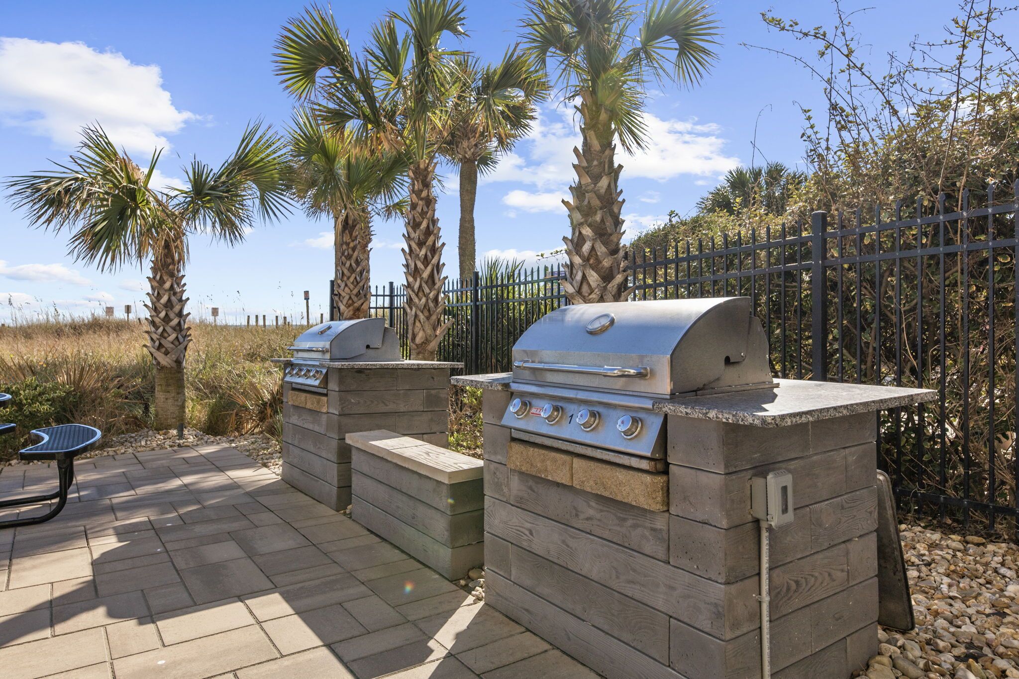 Une terrasse extérieure dotée de deux barbecues encastrés, d’une table de pique-nique et, en arrière-plan, de palmiers.