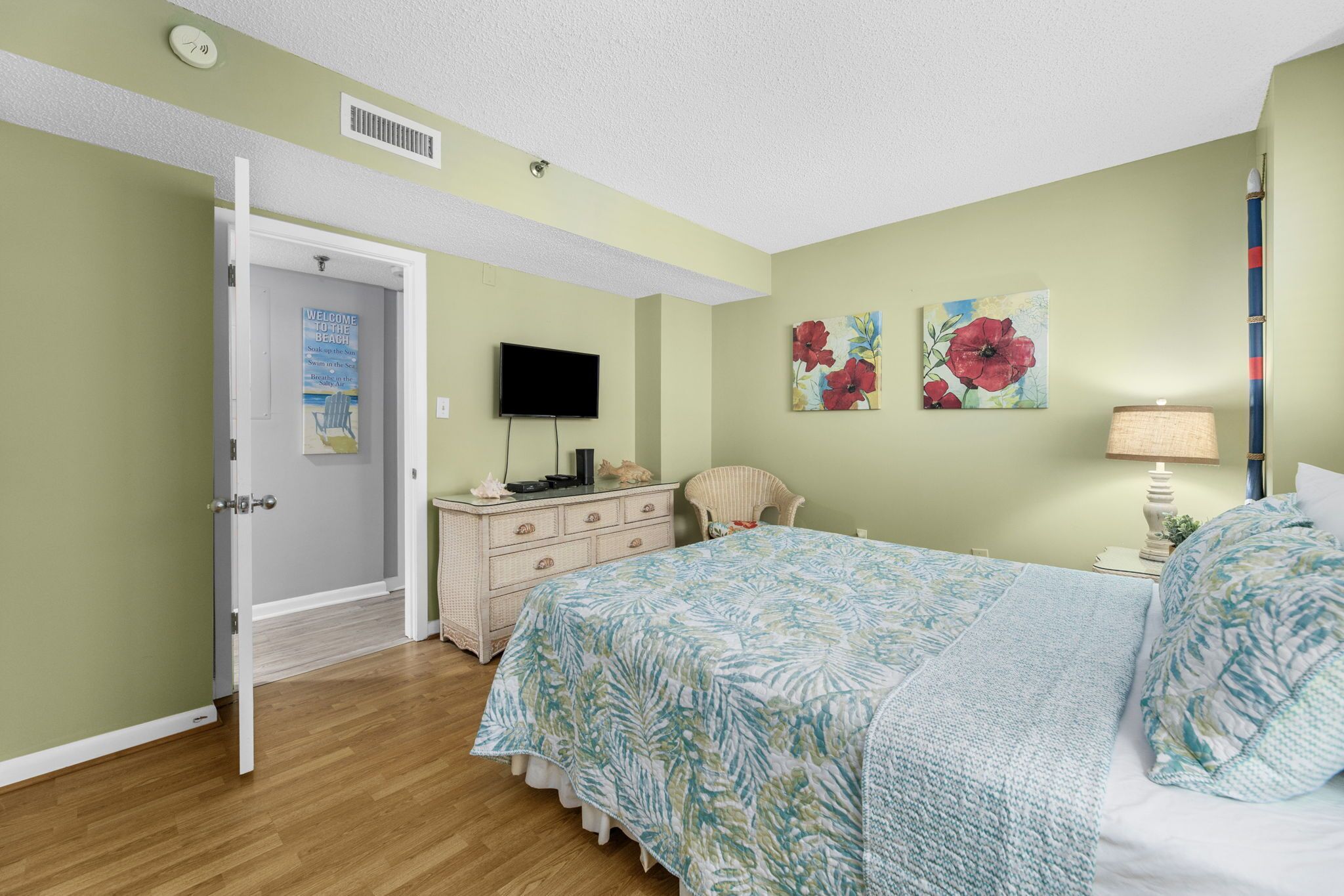 A bedroom with a bed, a dresser, a chair, a television, and a door.