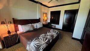 A hotel room with a large bed, a nightstand with a lamp, a ceiling fan, and a window with dark curtains. - AMAZING PRIME OCEANVIEW 2 BDRM, 3 BATH PENTHOUSE (Kapaa)