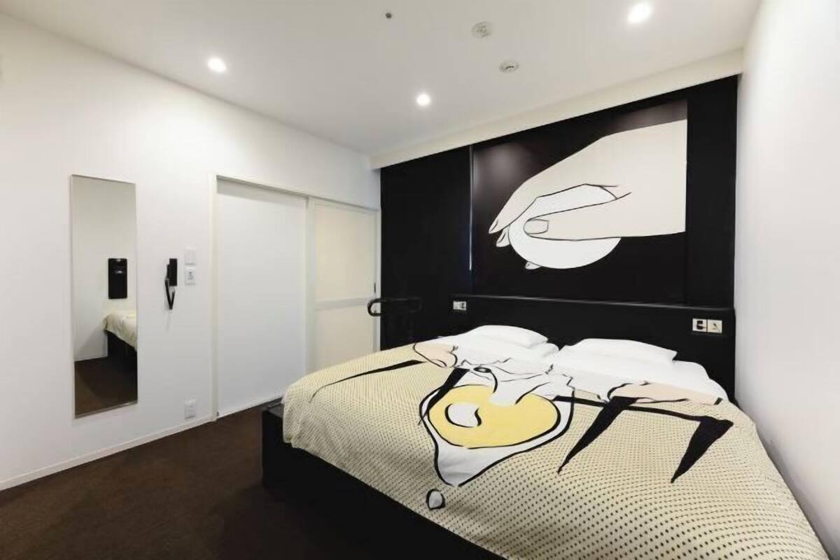 A hotel room with a bed, a large mirror, a wall-mounted artwork, and a door.