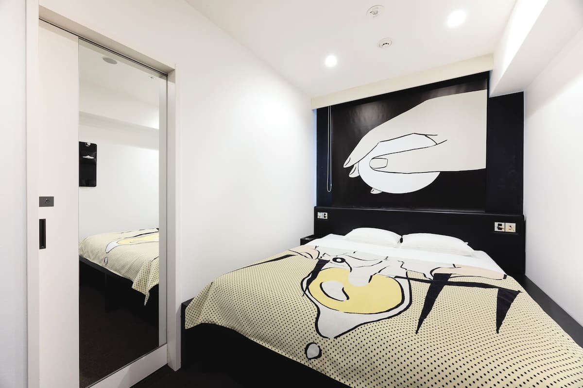 A modern hotel room with a bed, a large mirror, and a wall-mounted artwork.