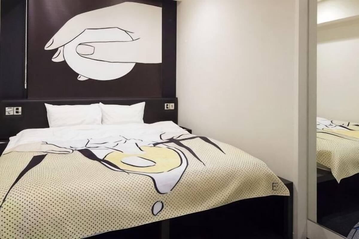 A hotel room with a bed, a large wall art piece, and a mirror.