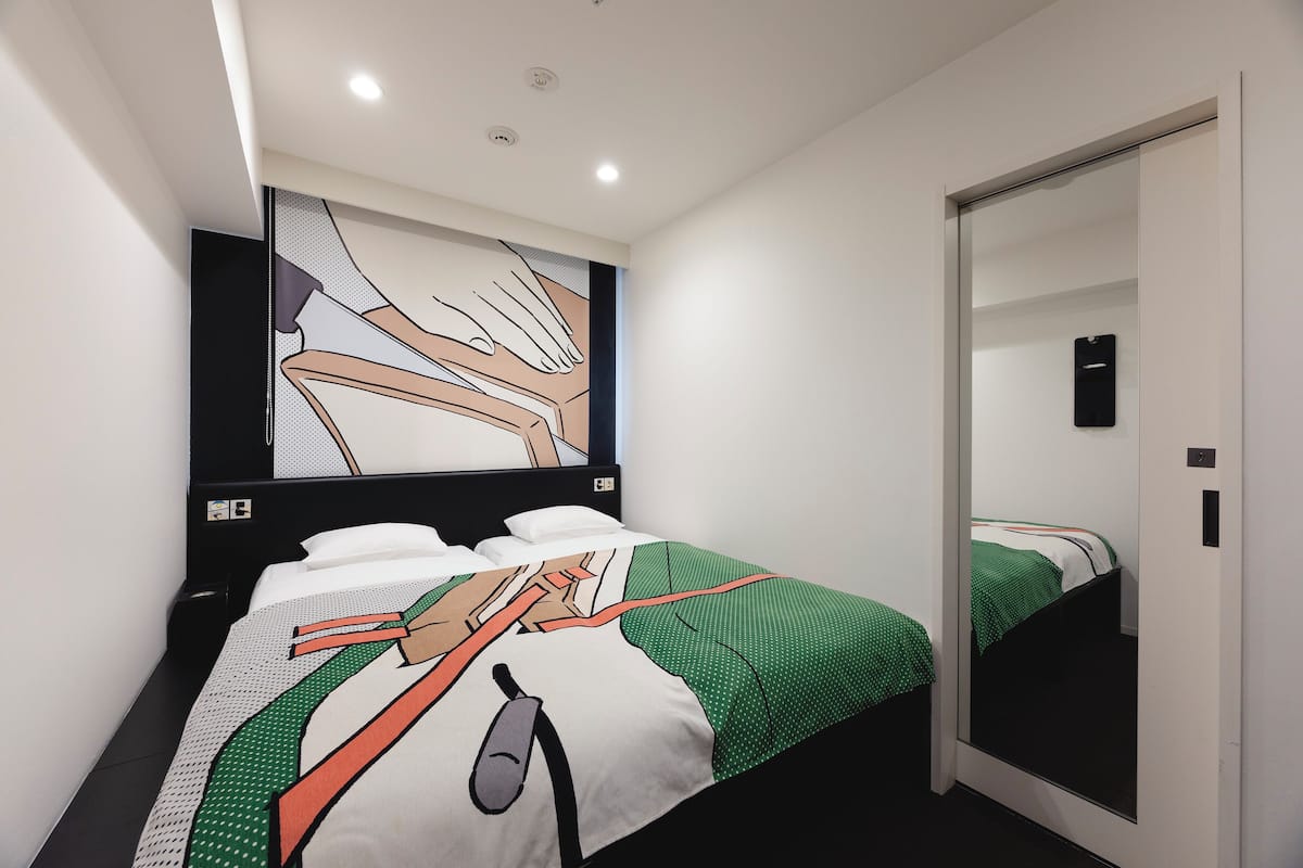 A hotel room with two beds, a large abstract painting on the wall, and a mirror on the door.