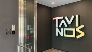 An elevator with a glass door, a wall-mounted sign reading "TAVINOS", and a fire alarm panel. - HOTEL TAVINOS Hamamatsucho (Tokyo)