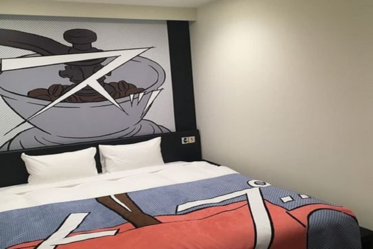 Une chambre d’hôtel comprenant un lit, une tête de lit agrémentée d’un panneau décoratif et une œuvre d’art fixée au mur.