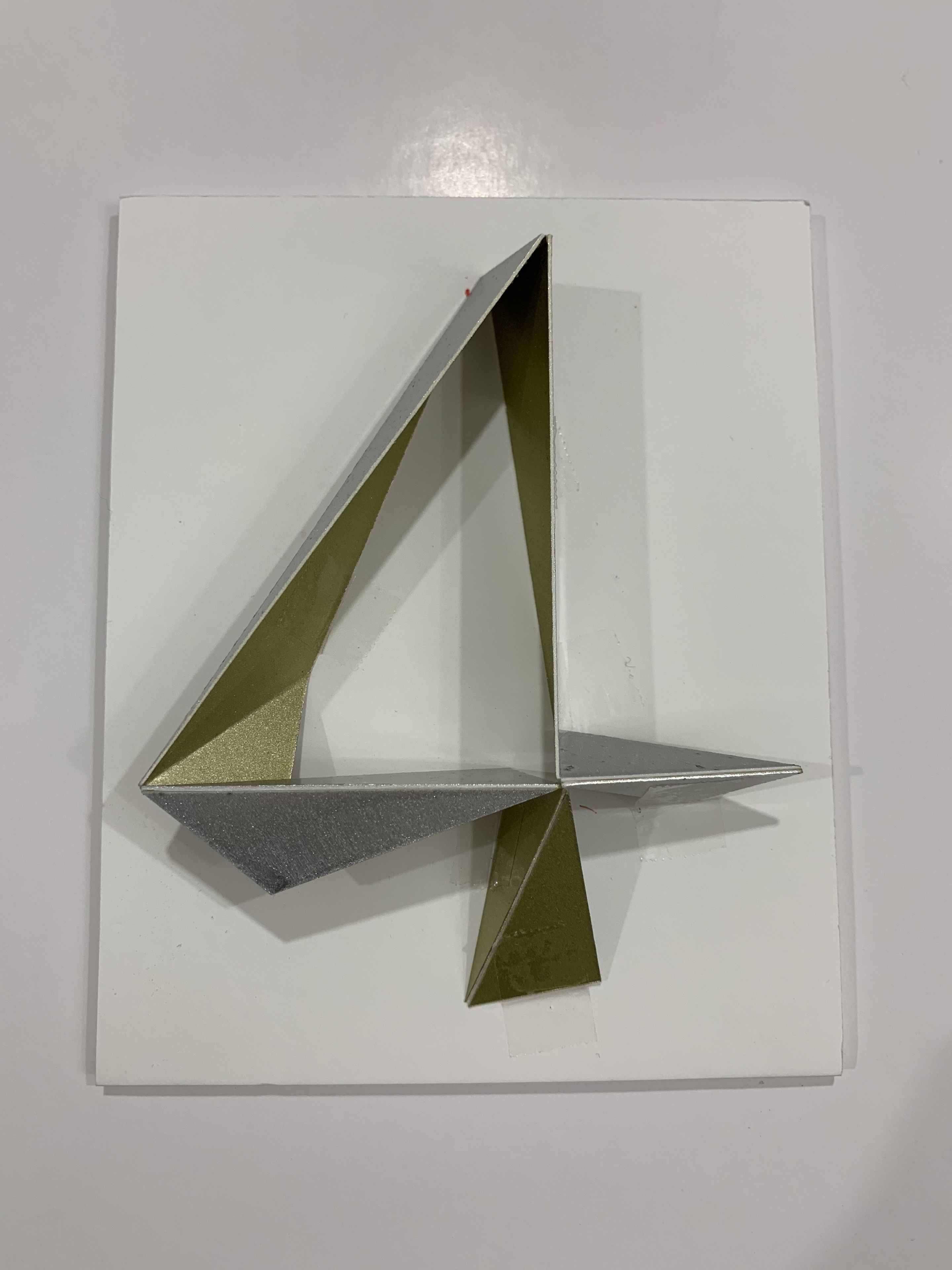 Escultura geométrica com acabamento metálico, montada sobre um fundo branco.