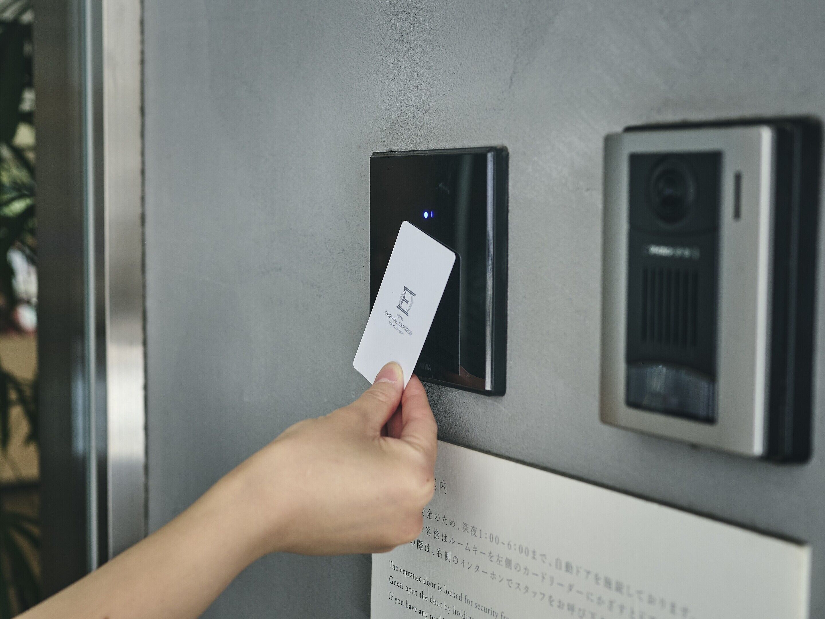 A hand holding a card near a card reader on a metallic surface, likely part of a hotel room's entry system.