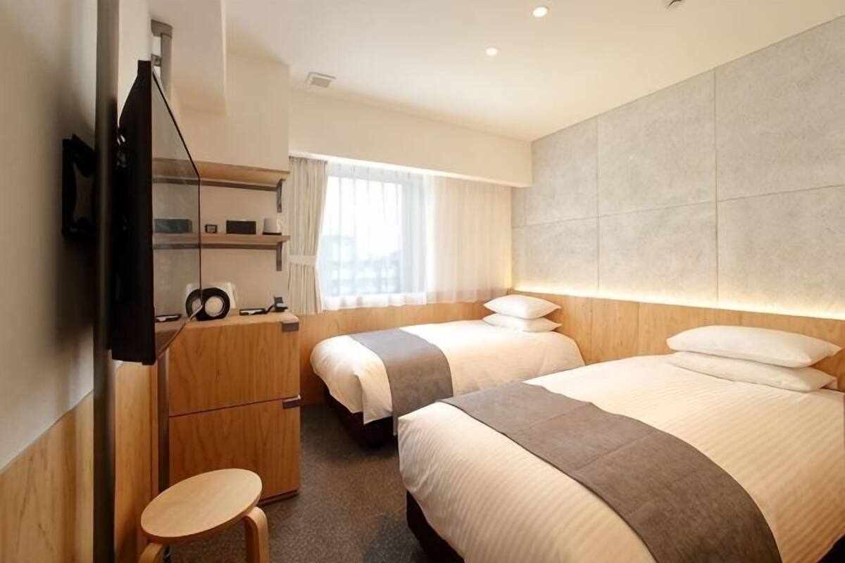 A hotel room with two beds, a desk, a chair, a TV, and a window with curtains.