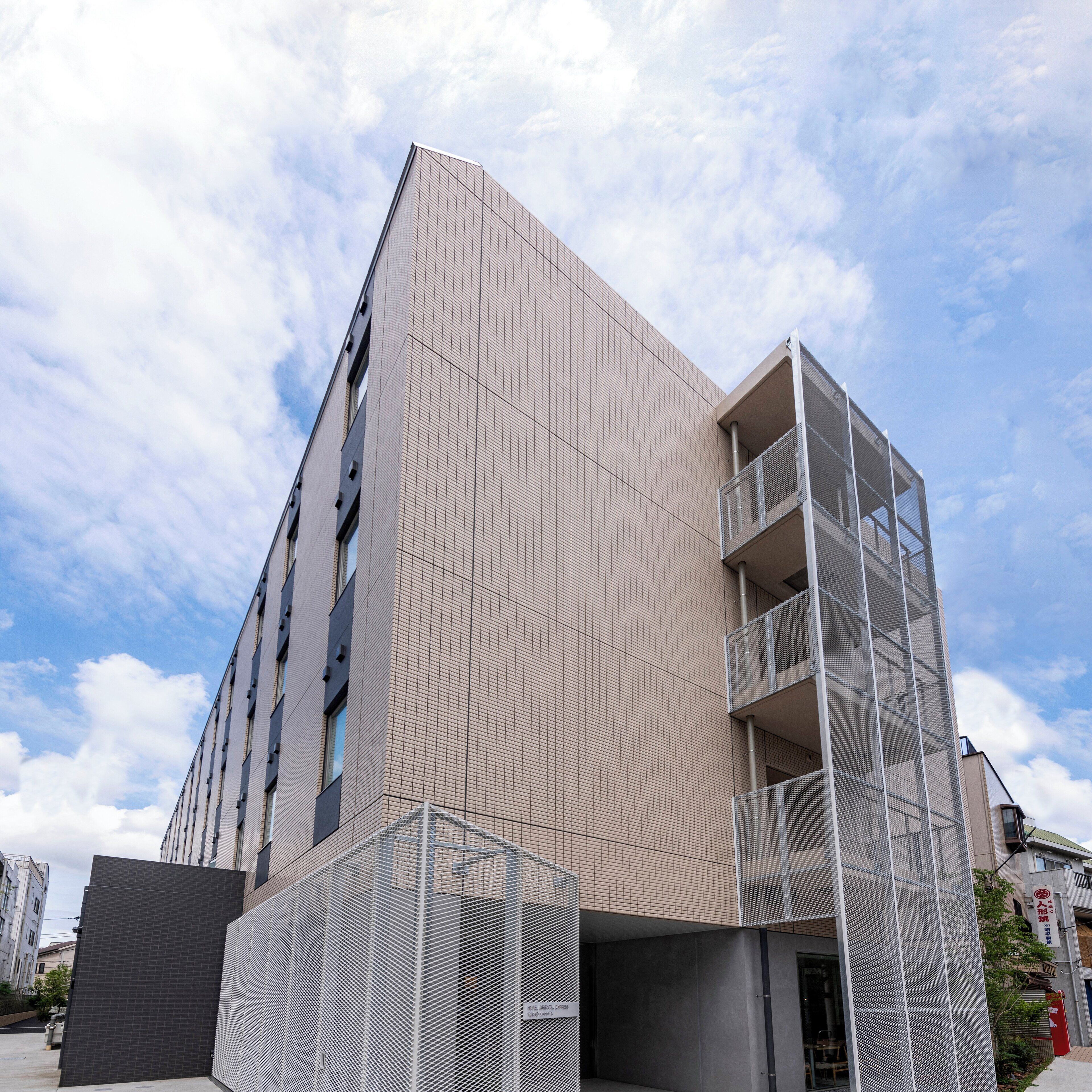 Un bâtiment moderne à la façade ornée d’un motif en réseau, avec une entrée bien visible et un balcon situé sur le côté droit.