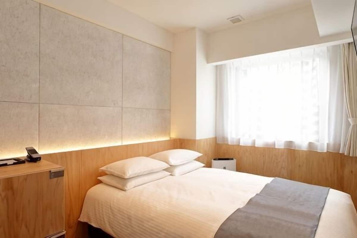 A modern hotel room with a large bed, a bedside table with a phone, and a window with curtains.