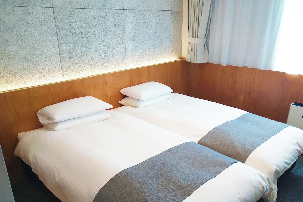 A double bed with white linens and gray accents, wooden headboard, and a stone wall.