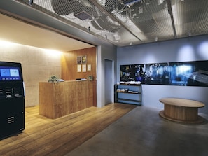 A reception area with a wooden desk, a digital kiosk, and a wall-mounted shelf with items. - Hotel Oriental Express Tokyo Kamata (Tokyo)