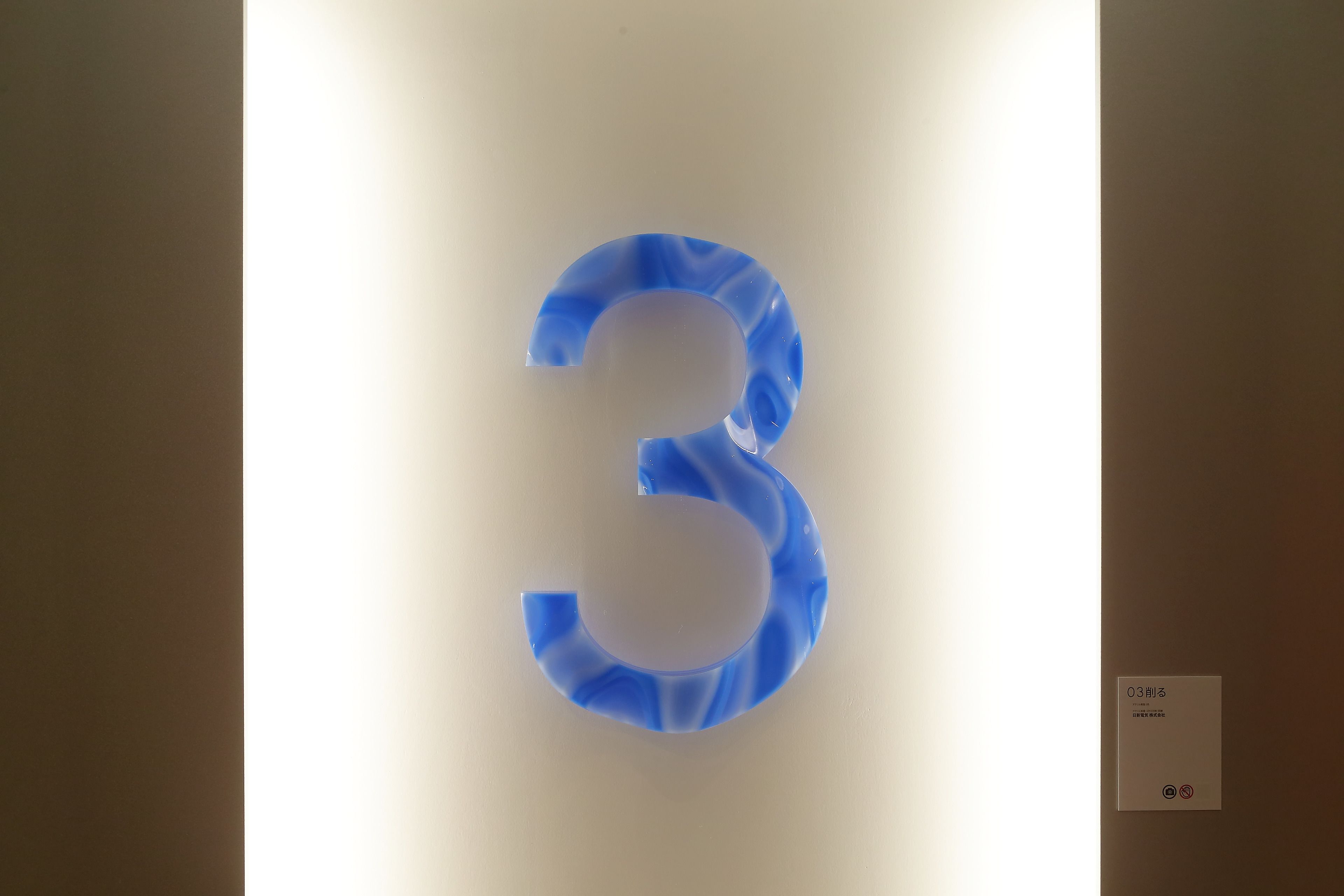 A wall-mounted number '3' with a light source behind it.
