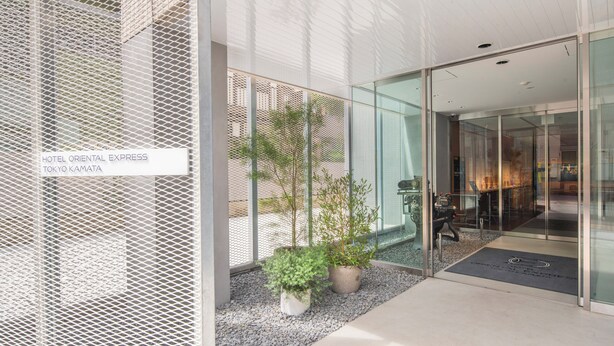 The entrance of Hotel Oriental Express in Tokyo Kamata, featuring a modern glass facade, potted plants, and a clear view of the interior. - Hotel Oriental Express Tokyo Kamata (Tokyo)