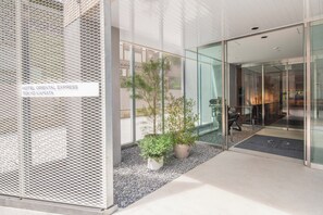 L’entrée de l’hôtel Oriental Express à Tokyo-Kamata se distingue par sa façade moderne en verre, ses plantes en pot et une vue dégagée sur l’intérieur.