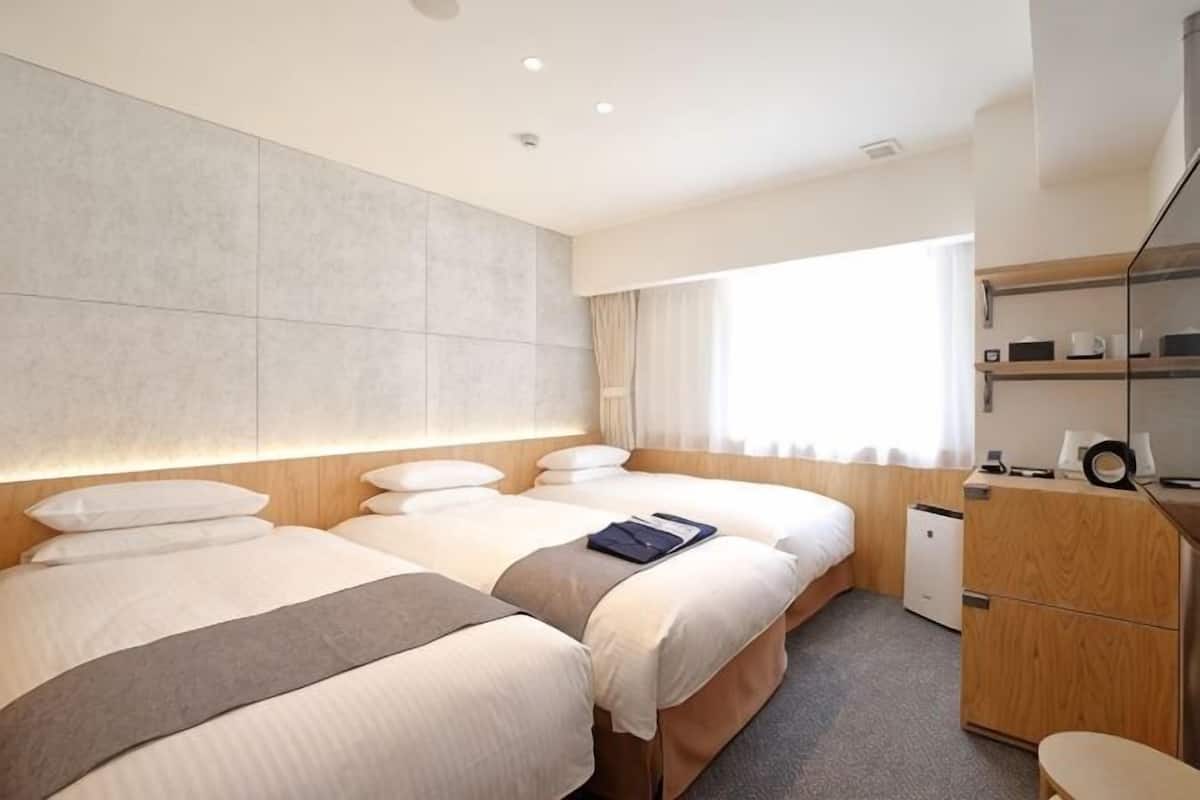 A hotel room with two beds, a wooden headboard, a desk, a chair, and a window with curtains.