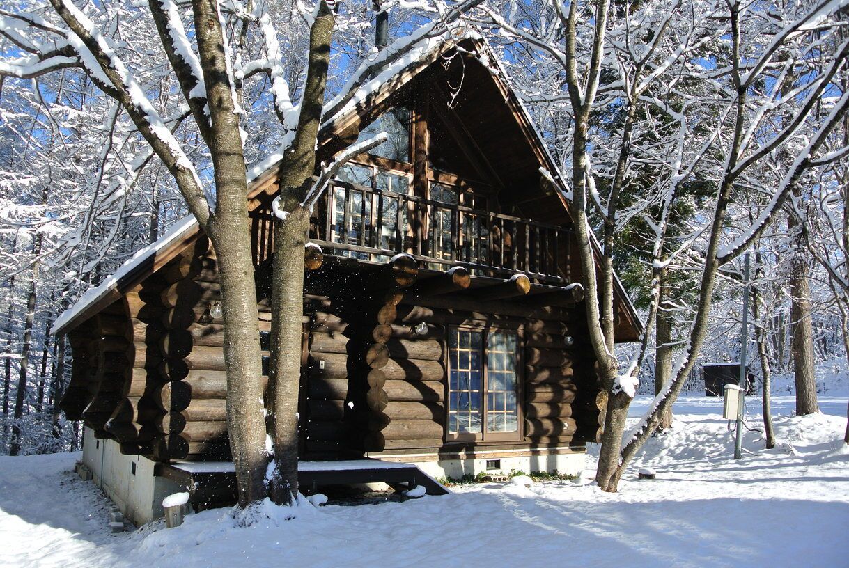 Una cabaña de madera con balcón, rodeada de árboles cubiertos de nieve.