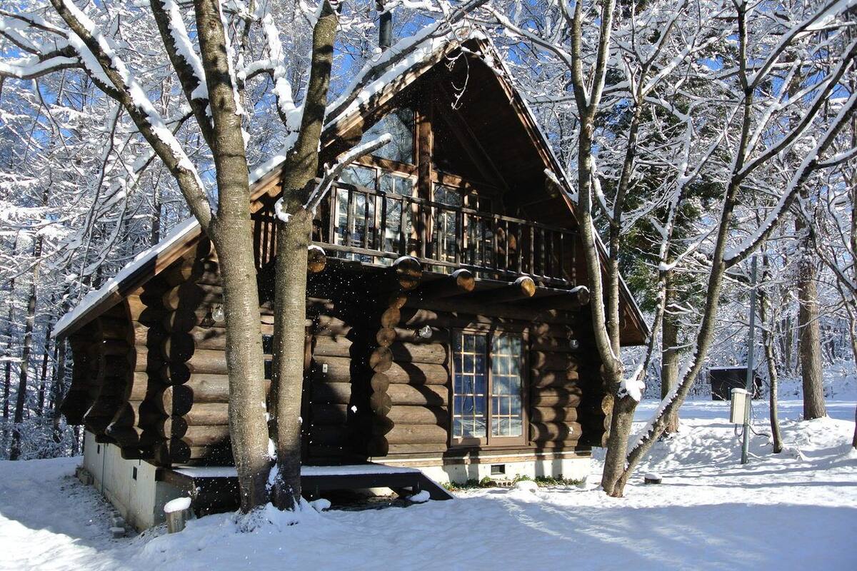 Una cabana de fusta amb un balcó, envoltada d'arbres coberts de neu.
