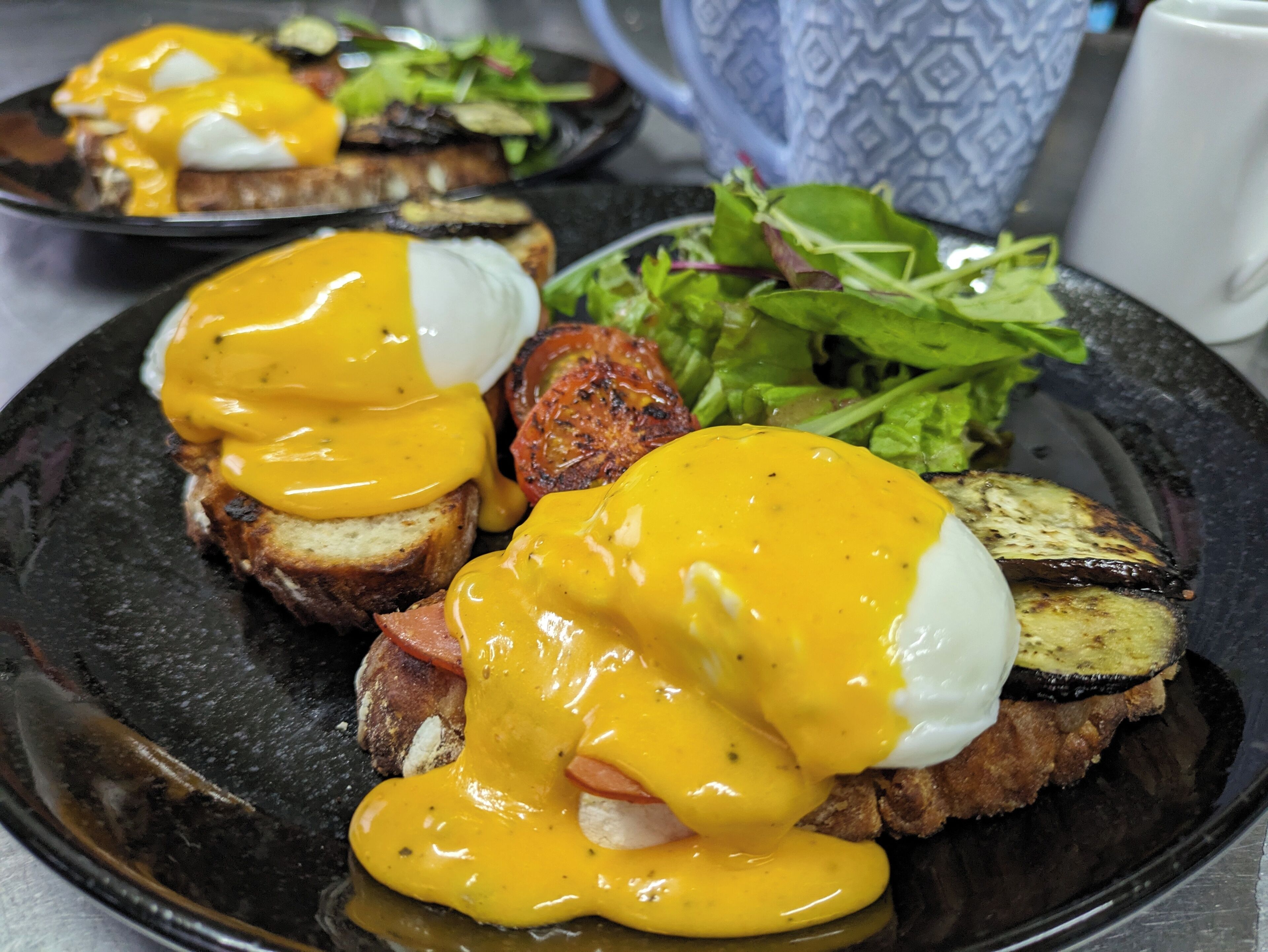 A breakfast plate with eggs benedict, bacon, grilled tomatoes, and greens.