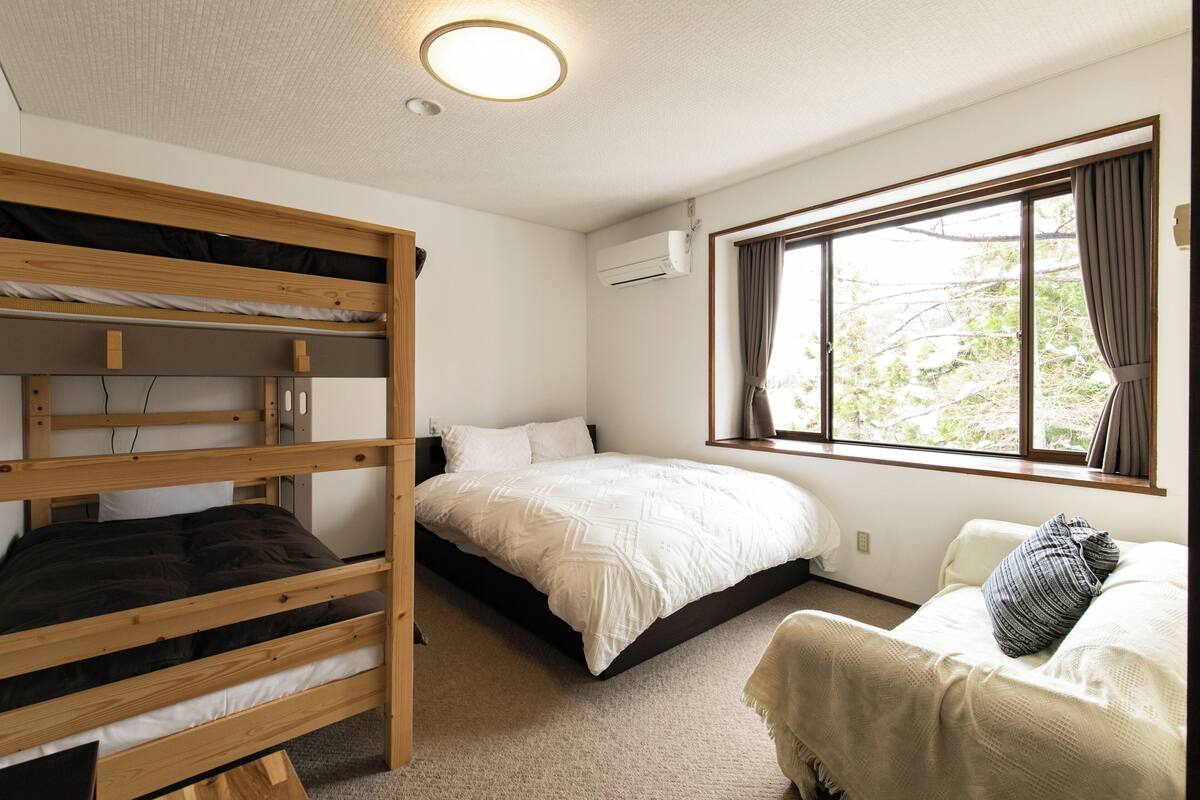 Habitació amb lliteres, un llit individual, una finestra amb cortines i un aparell d'aire condicionat.
