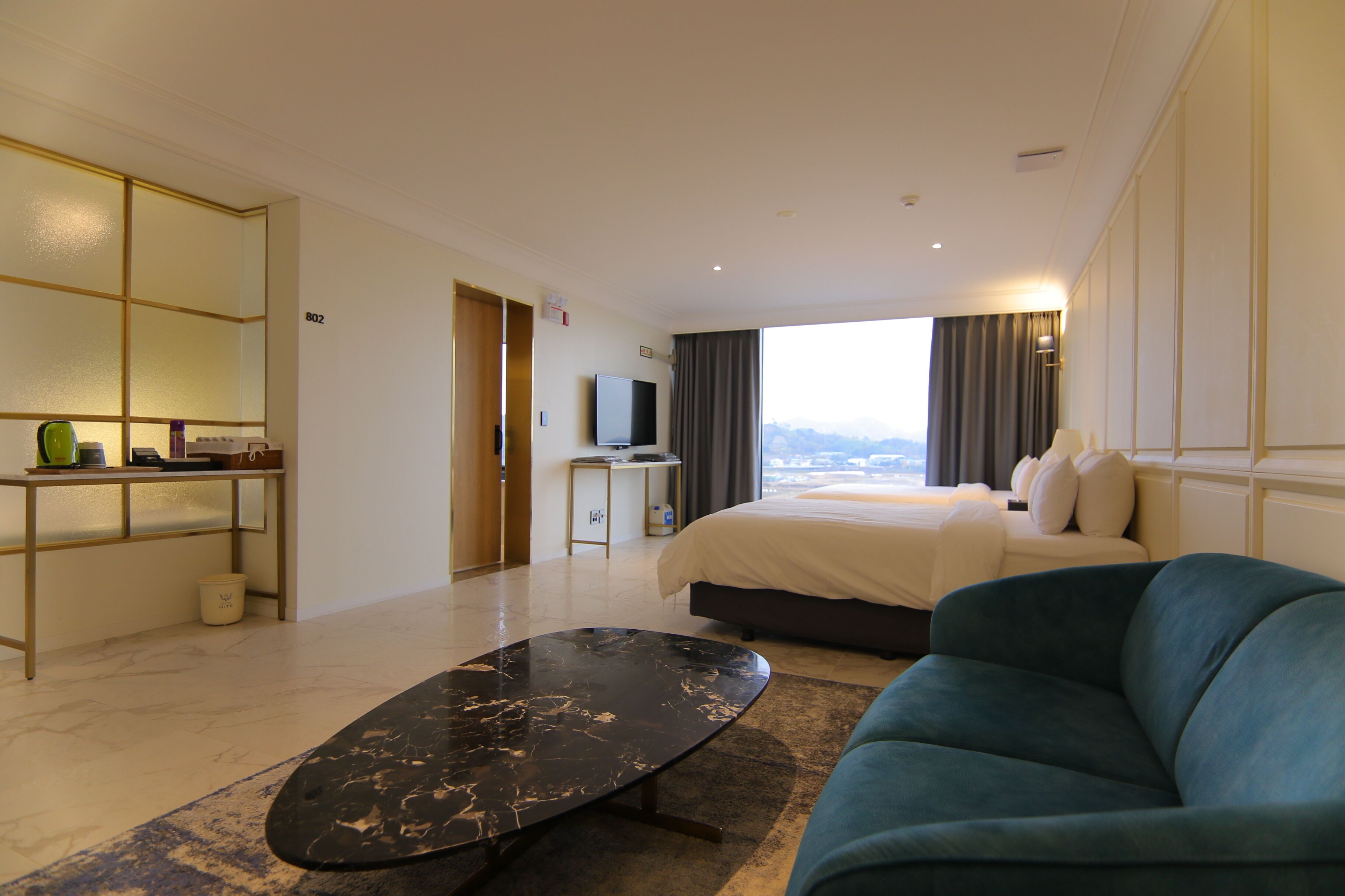 A hotel room with a bed, a blue sofa, a television, a desk, and a view of the mountains.