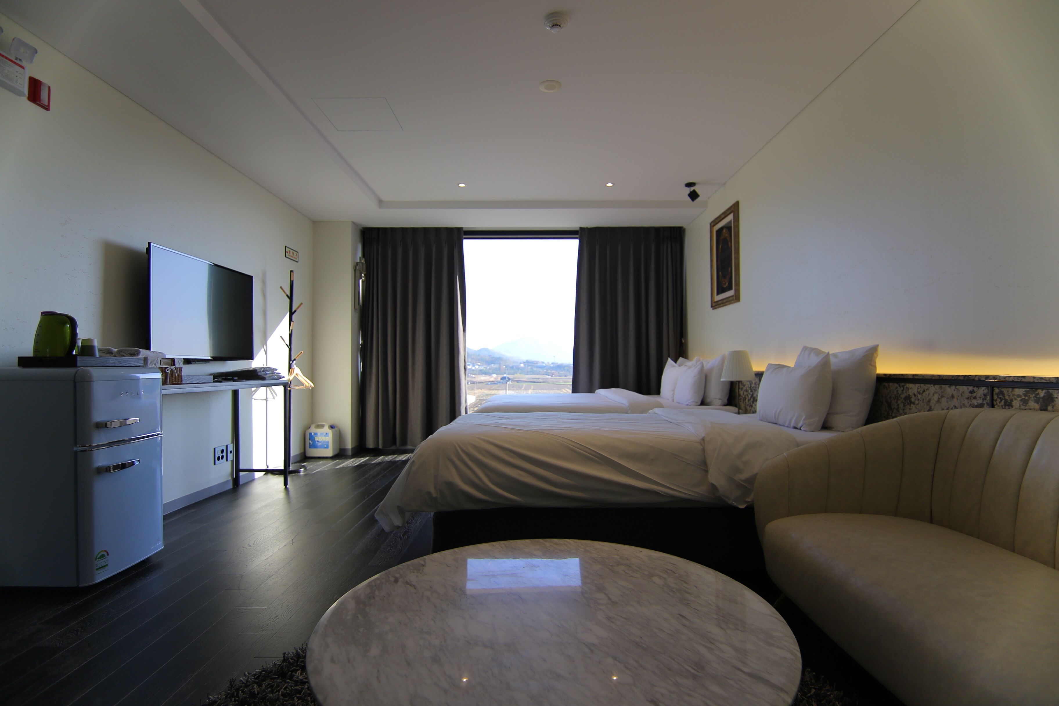 A hotel room with a bed, a desk, a television, and a view of the city.