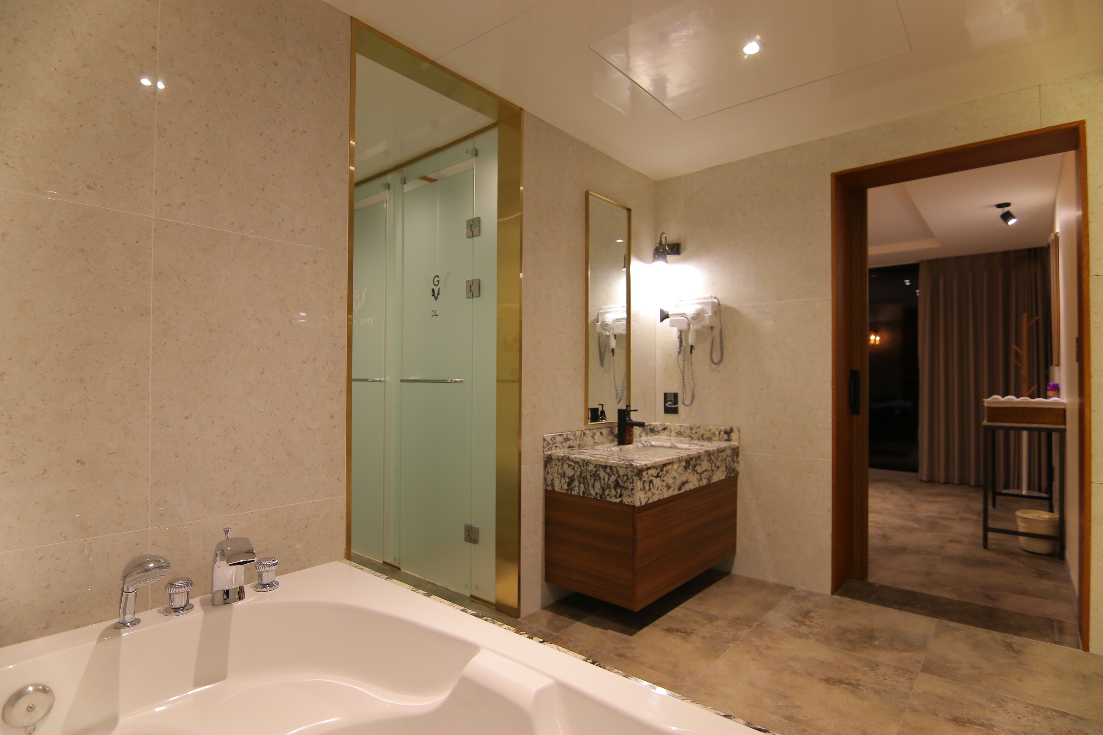 Une salle de bain moderne dotée d’une grande baignoire, d’un meuble-lavabo avec un plan de travail en marbre et d’une cabine de douche en verre.