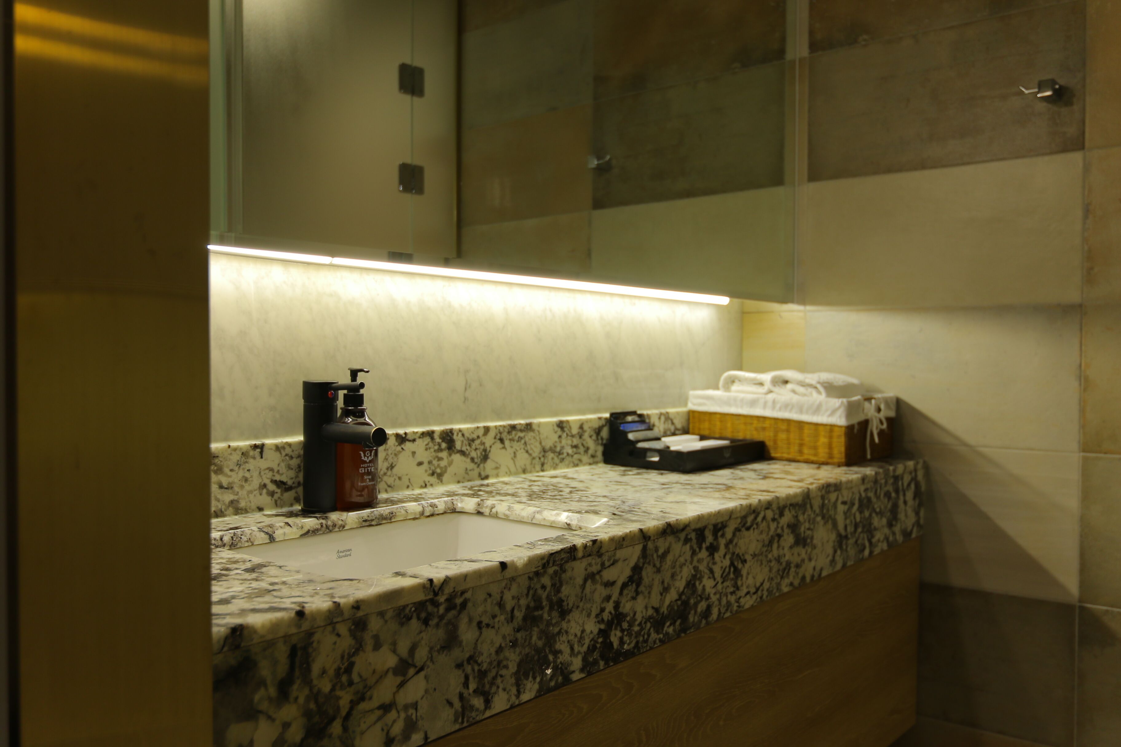 Baño con encimera de mármol, lavamanos, espejo, dispensador de jabón y caja de pañuelos.