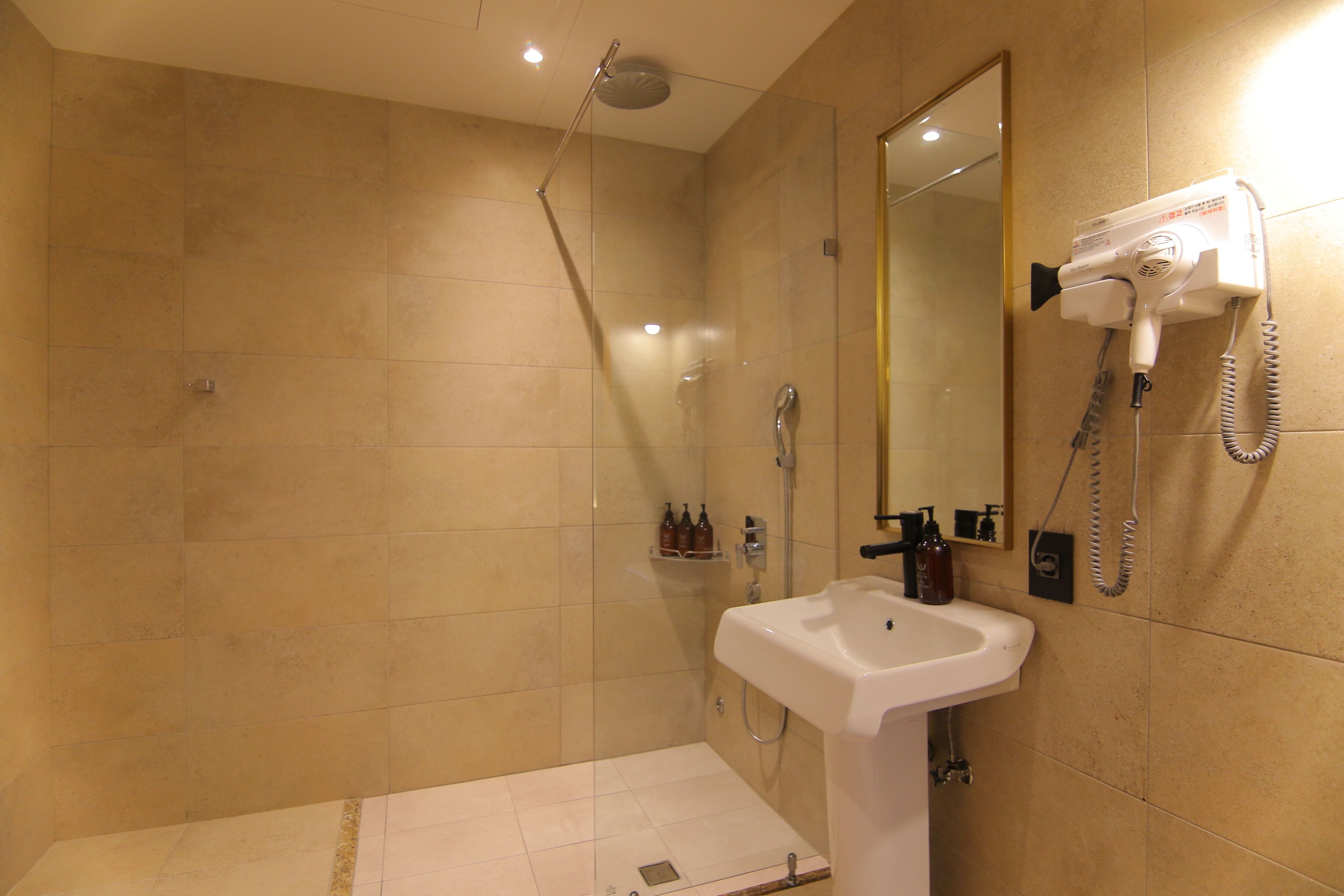 A bathroom with a shower, a sink, and a hairdryer mounted on the wall.