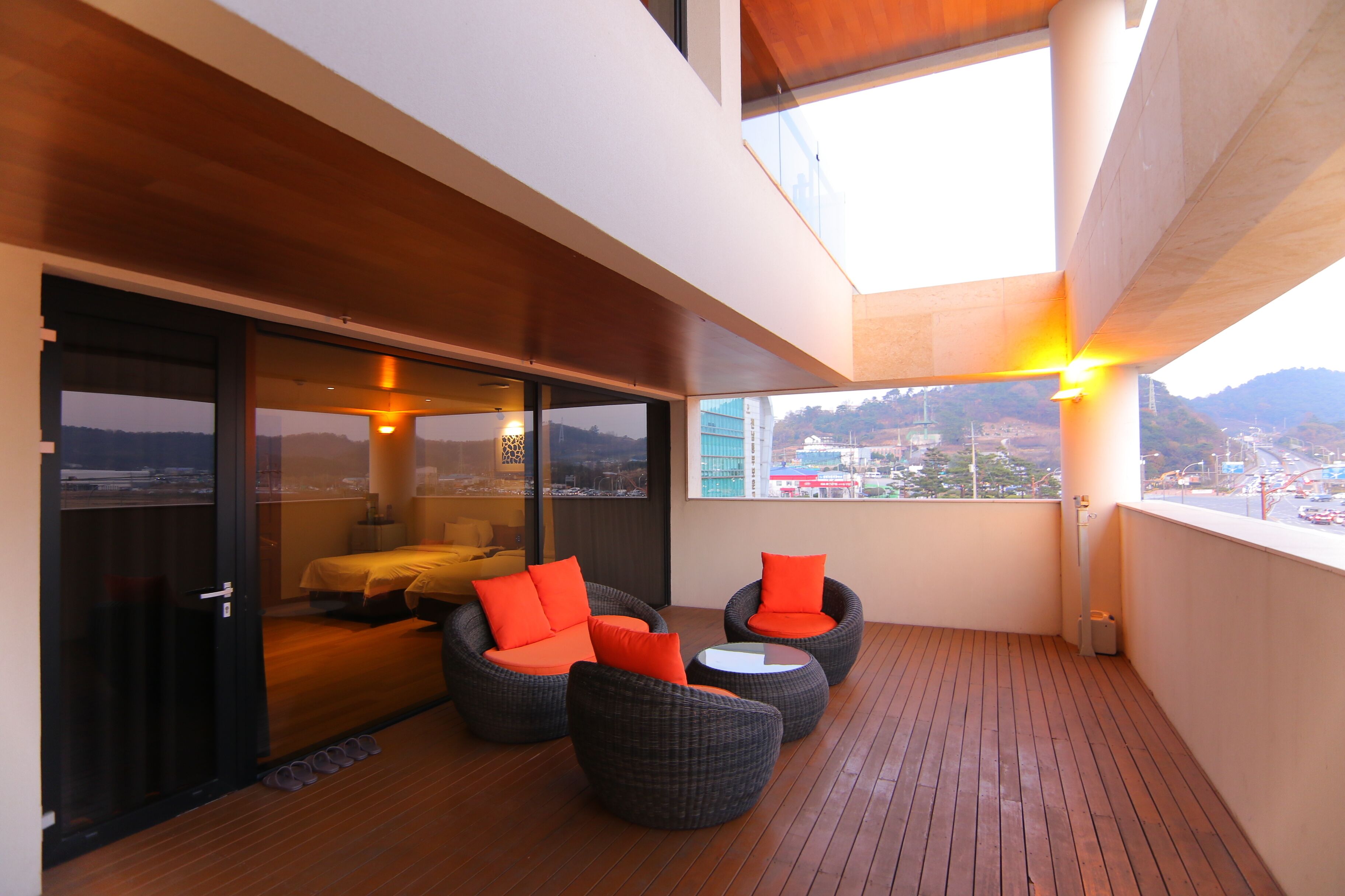 A balcony with wicker furniture and a bed, large windows, and a view of a cityscape.