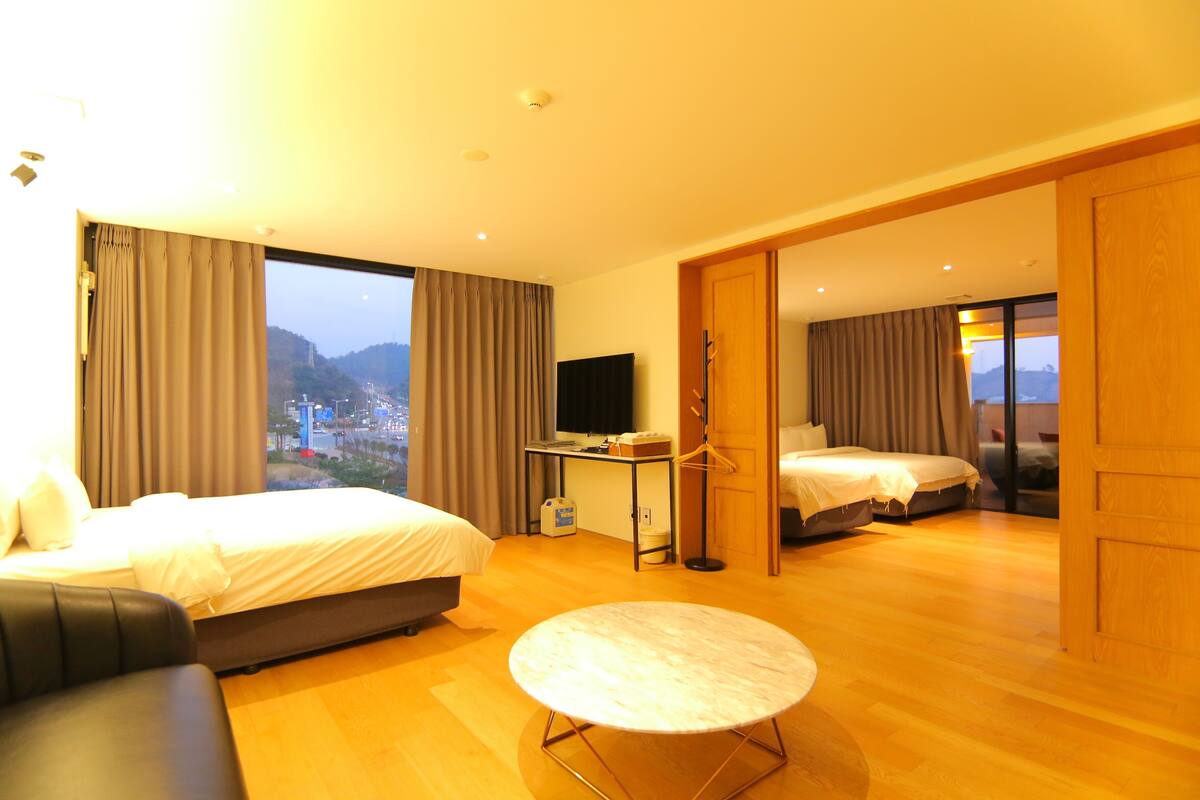Habitación de hotel con cama, sofá, televisión y vistas a un paisaje urbano.