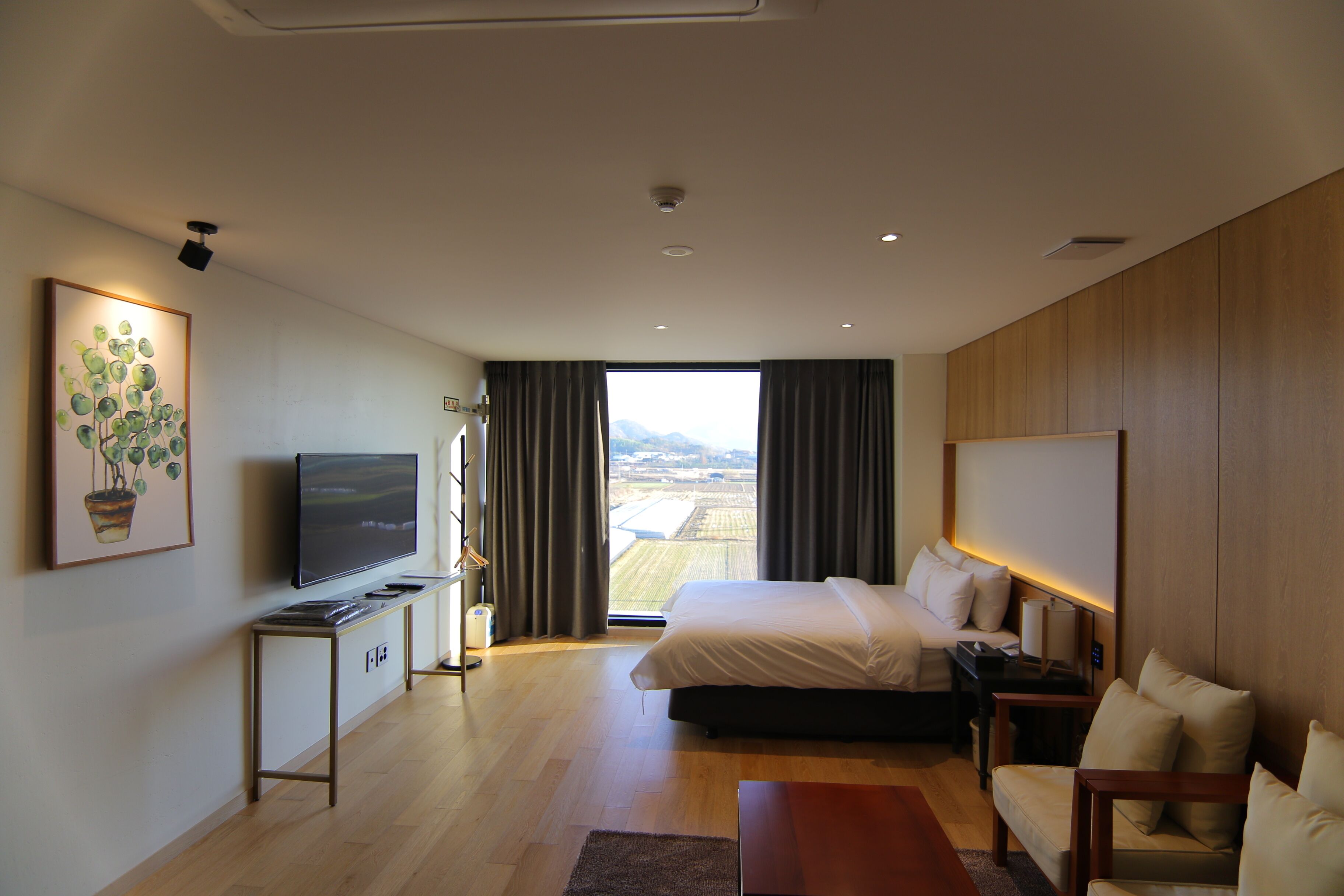 A modern hotel room with a large bed, a TV, a desk, and a view of the city.