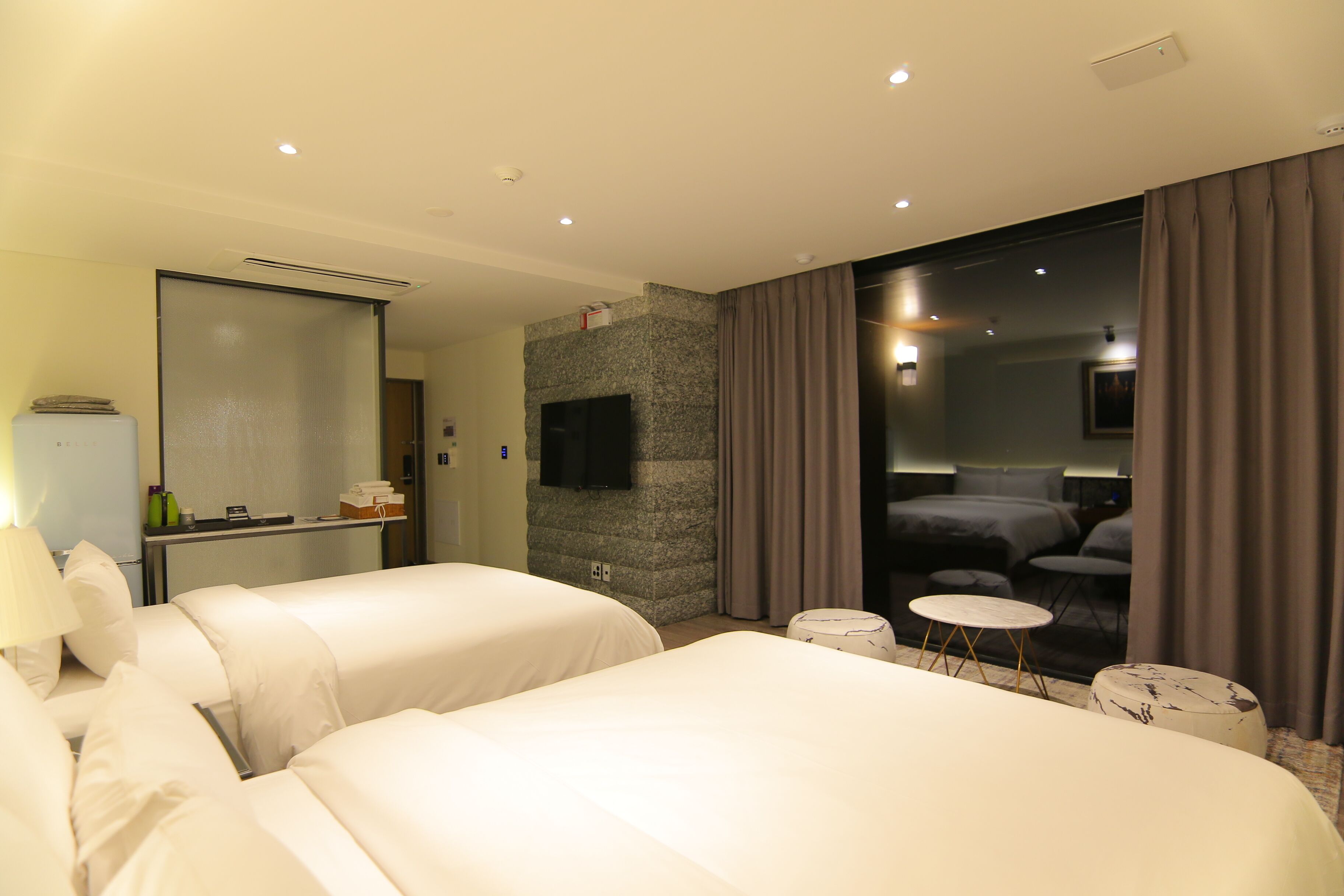 Une chambre d’hôtel avec deux lits, une télévision, un mur en pierre, une salle de bain et une vue sur une autre chambre.