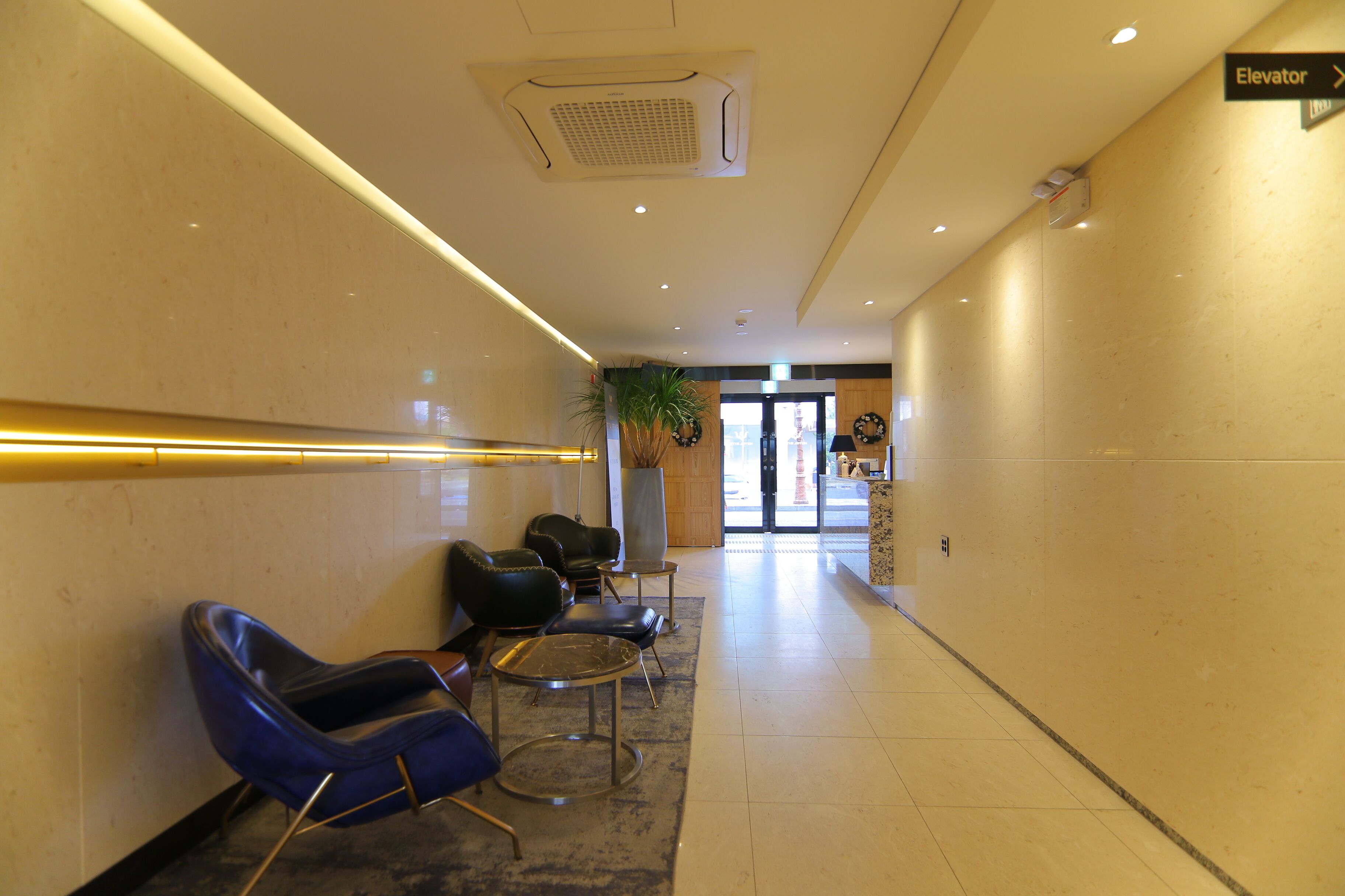 Un hall d’hôtel avec un long couloir, un comptoir d’accueil et un panneau indiquant l’ascenseur.