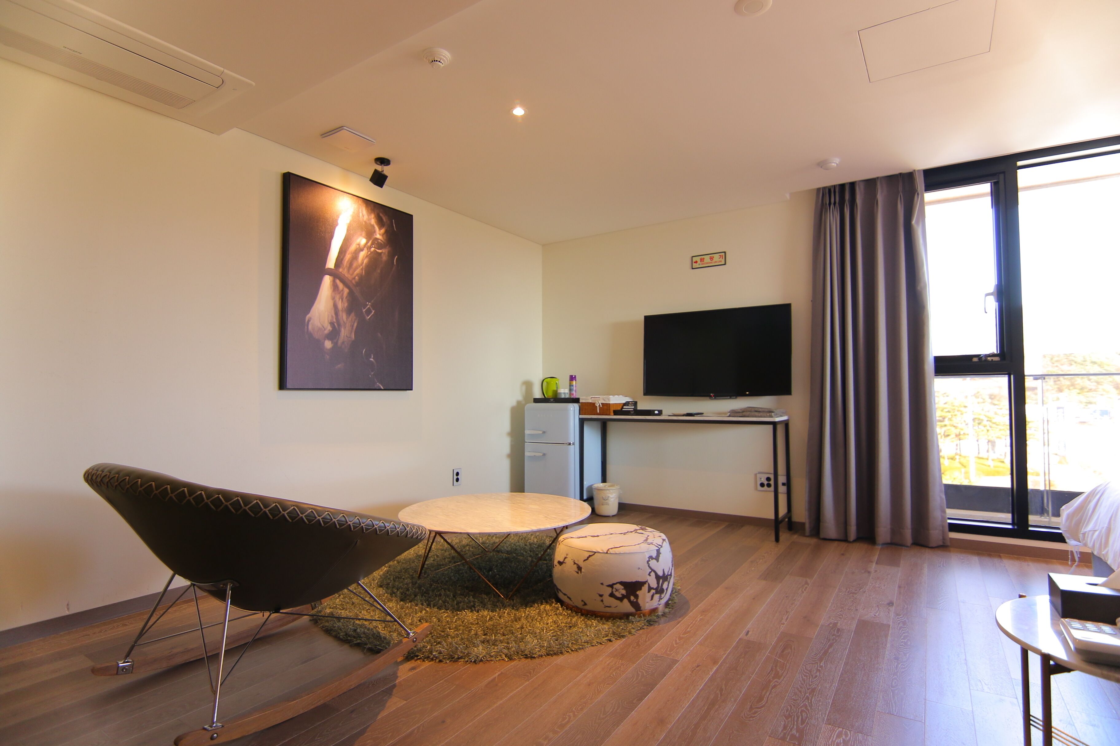A modern living room with a round table, a unique chair, a television, and a large window with curtains.